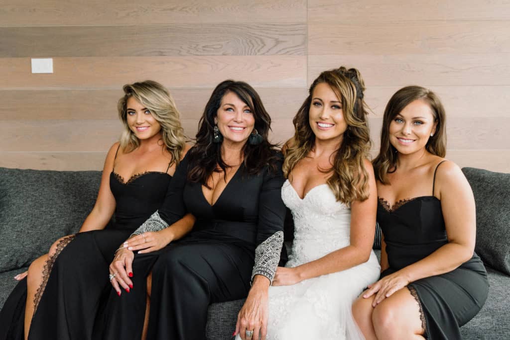 bride and bridesmaids sitting on bed in hotel before wedding captured by james white photography