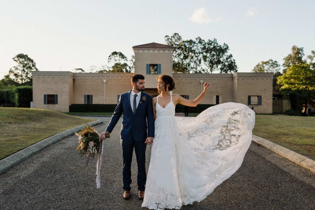 bride and groom stand in front of iconic estate tuscany villa as bride throws dress in the wind, captured by hunter valley wedding photographer james white