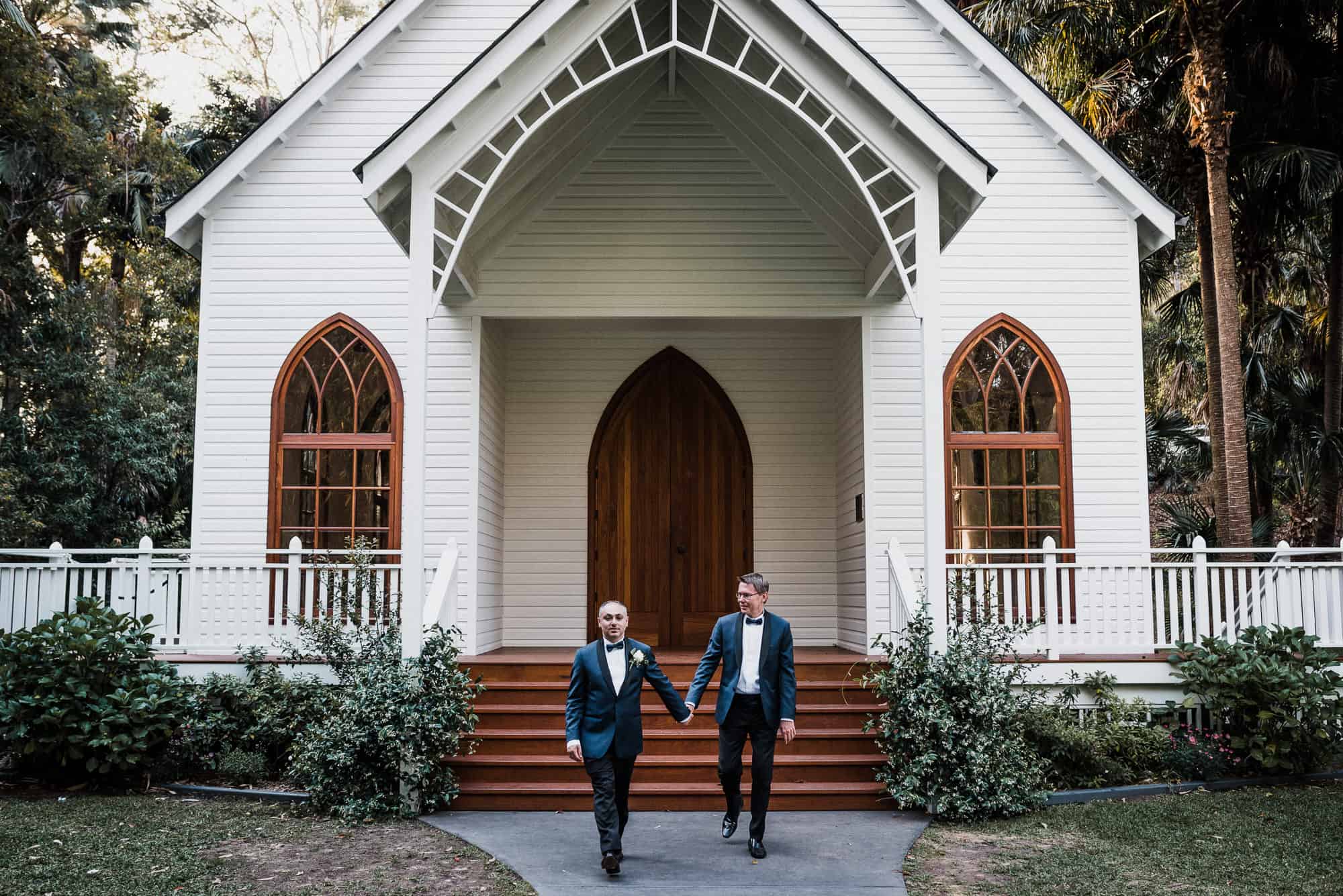 two grooms hold hands in front of vintage chapel at Kantara House