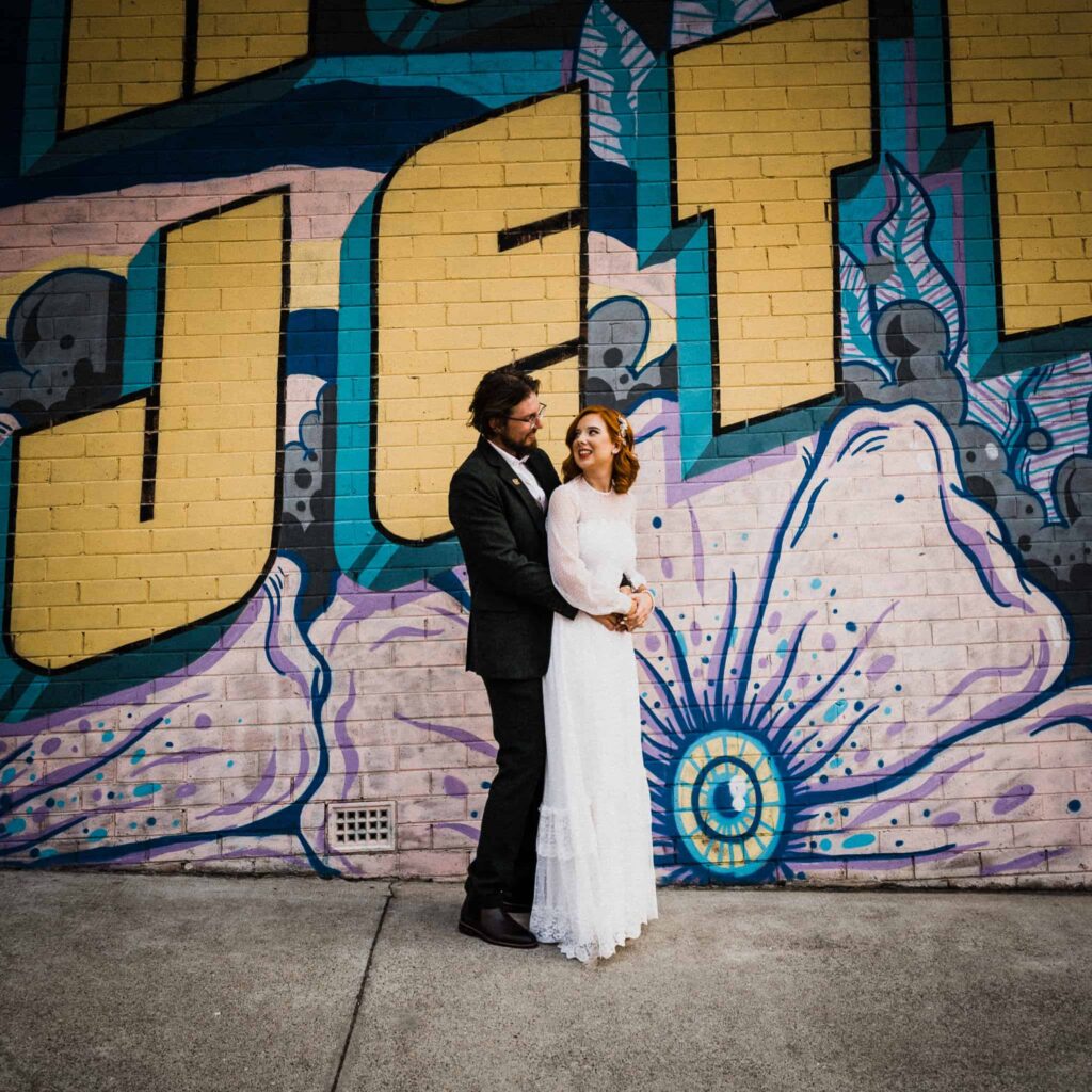 bride and groom pose against graffiti wall in long jetty the savoy long jetty wedding