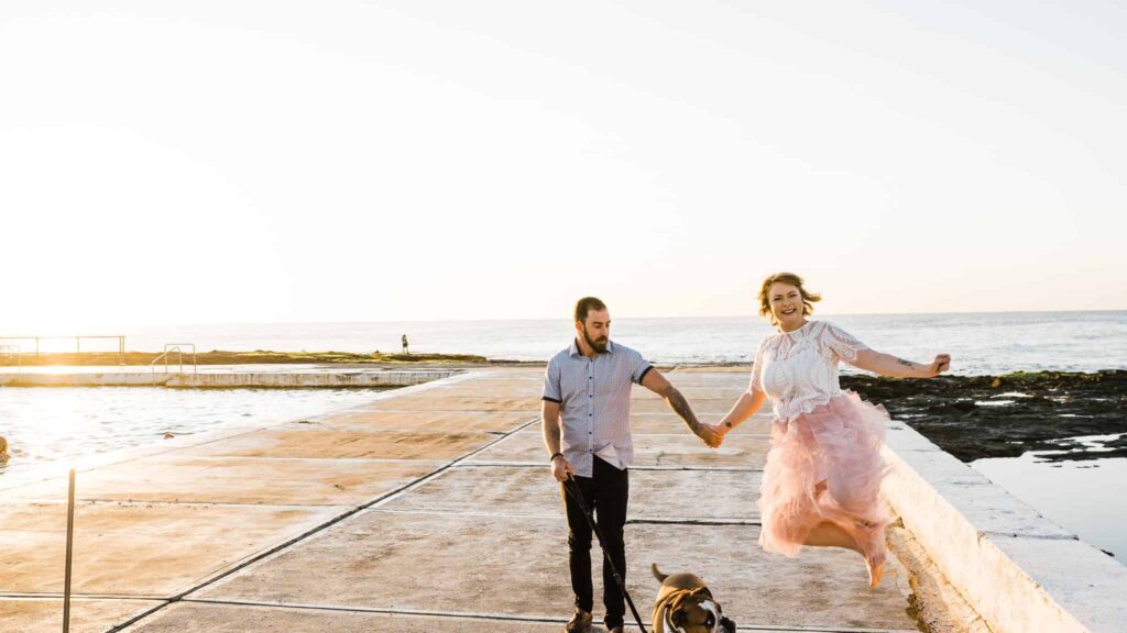 bride and groom jumping for joy at newcastle baths as they walk their dog before wedding captured by james white newcastle wedding photographer