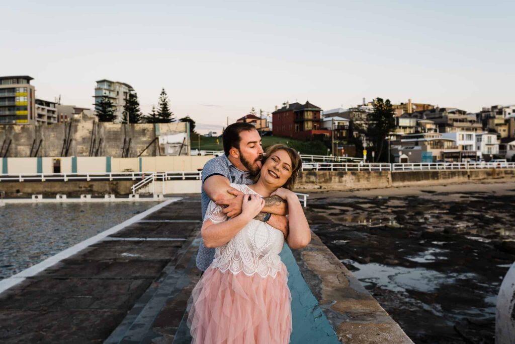 groom being silly licking brides face as they pose for portraits under the sun rising captured by james white newcastle wedding photographer