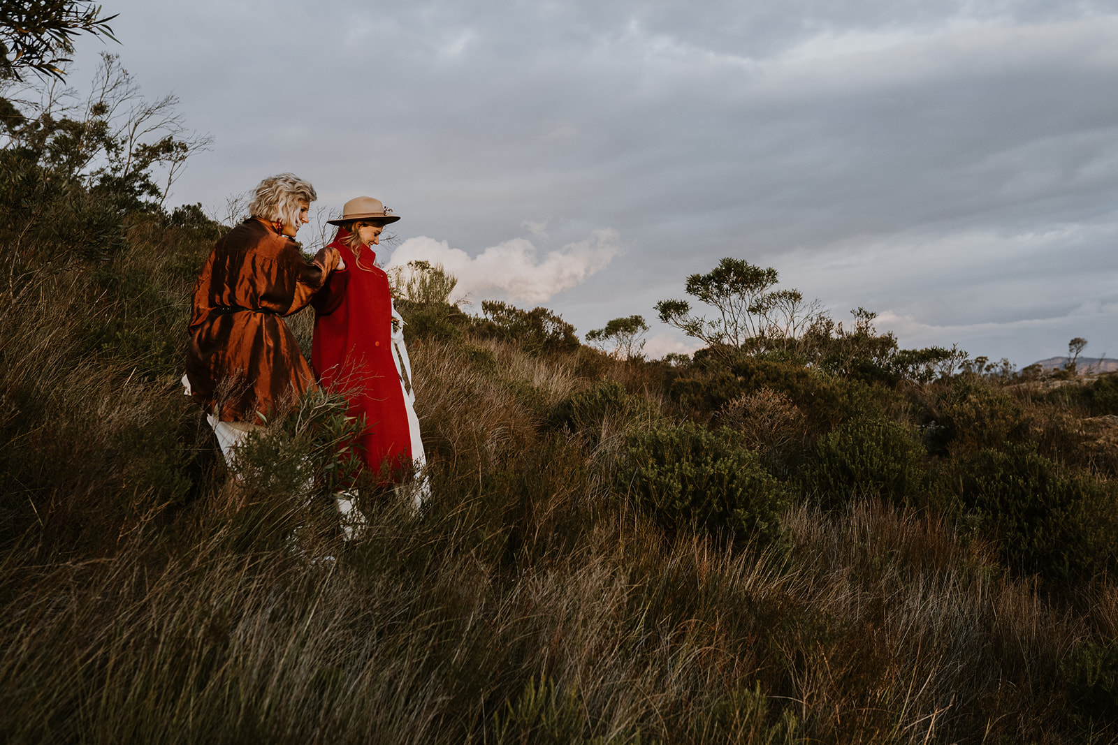 Both brides trek through the blue mountains, in colourful red overcoats as we film their intimate wedding film