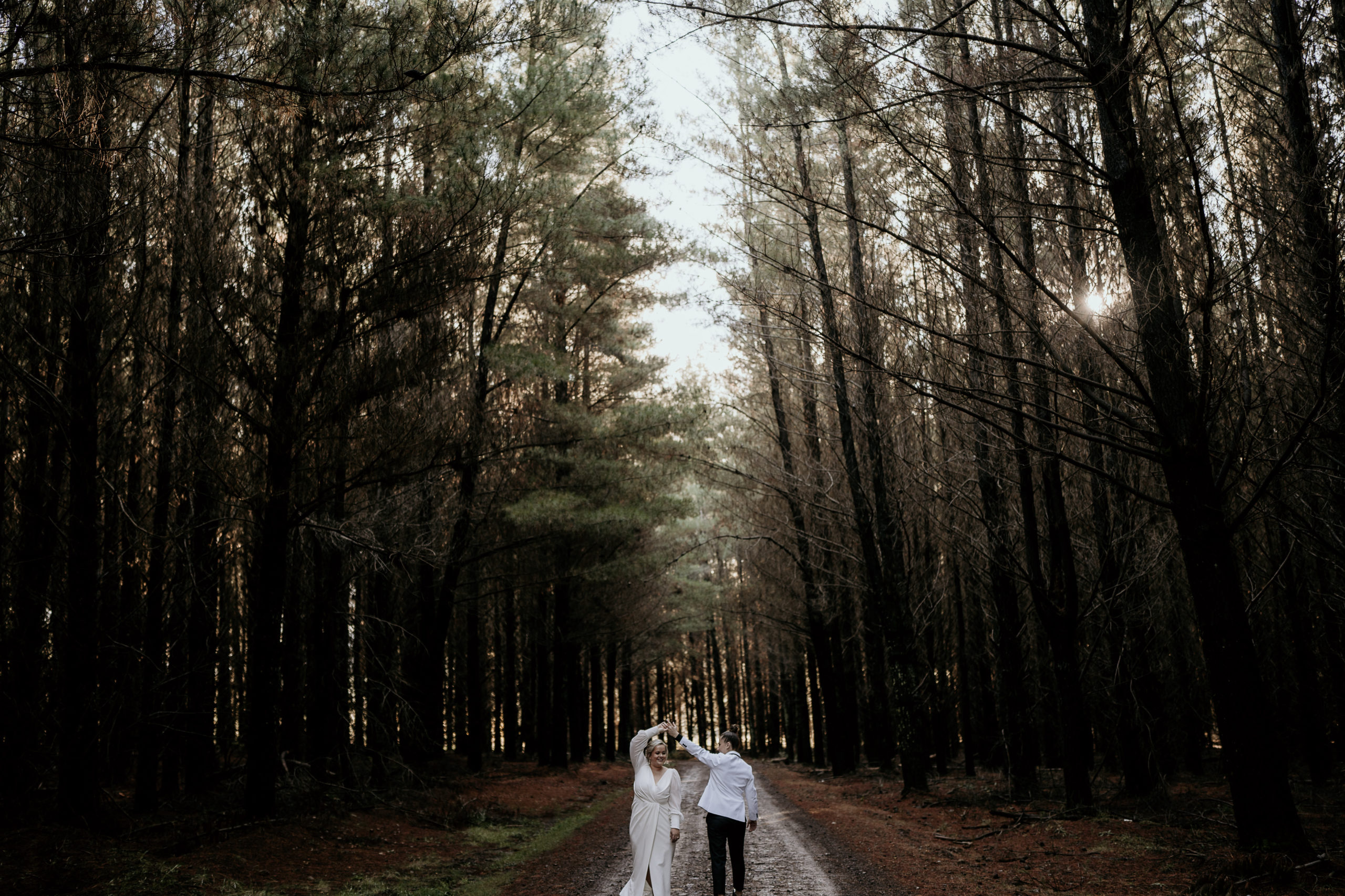 Both brides are dancing in a row of trees in the pine forest out in Orange during their intimate wedding film