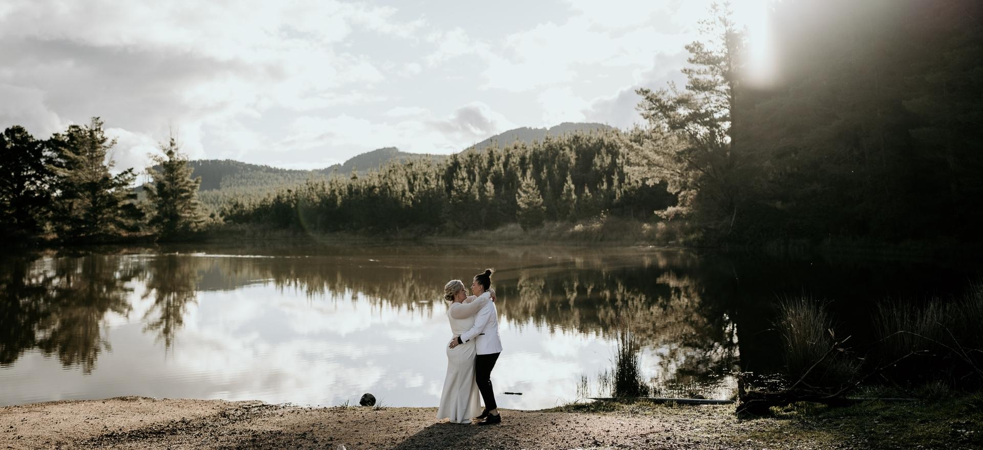 Brides embrace down by a lake during the filming of their intimate wedding