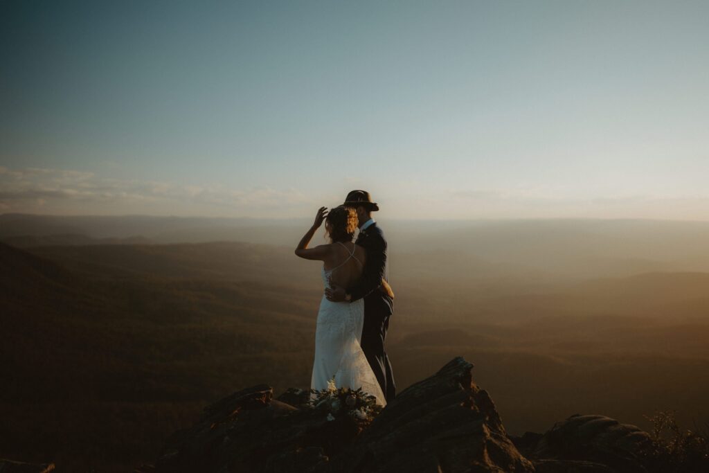 Bride and groom standing on the edge of an epic mountain in the Blue Mountains after their elopement ceremony. If you tell your family you're eloping, they should support you to have a day like this.