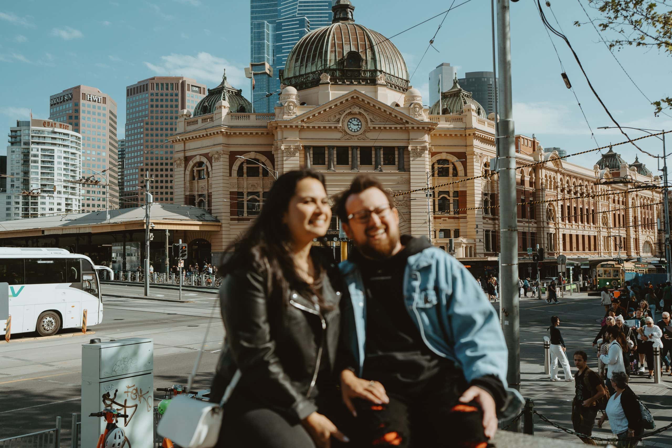 Couple sit in front of Flinders Street Station in Melbourne right before they walk down to the Yarra River to renew their vows without an officiant